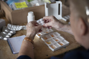 View of elderly woman putting pills into a weekly medication dispenser for mesothelioma pain