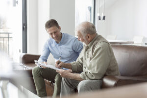 Senior citizen discusses his benefits with a Medicare advisor on a sofa