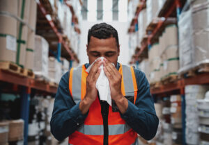 Young black man working in warehouse blows his nose into a tissue.