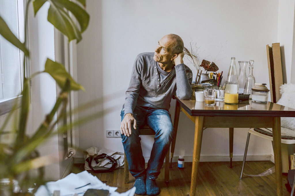 Mature man with mesothelioma distressing at dining table with plant in foreground