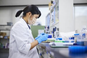 Woman with dark hair wearing gloves and a lab coat performing medical research