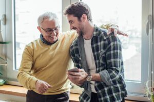 Older man weaing glasses and sweater putting his arm around young man in flannel