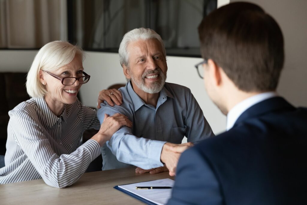 Mature man shaking hands with male lawyer while mature woman holds old man