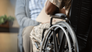 Injured African American Veteran in wheelchair talks with military doctor. Both men are seen from the neck down. Focus is on the man in the wheelchair. 